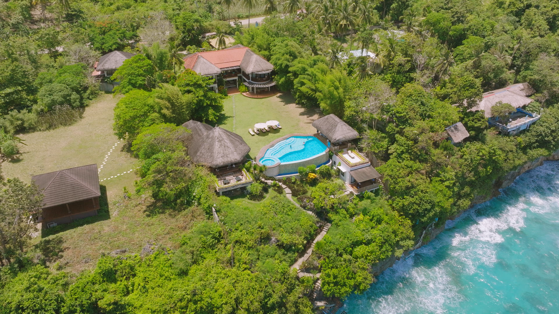 Aerial view of tropical resort with pool, ocean, and lush greenery.