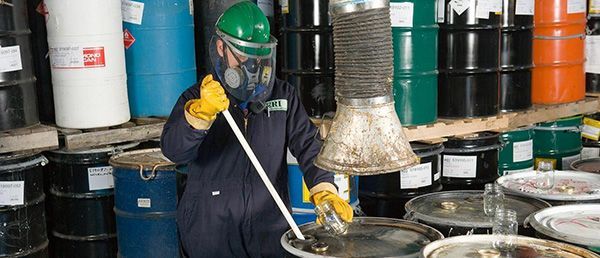 Un homme portant un masque à gaz et des gants mélange des produits chimiques dans un entrepôt.