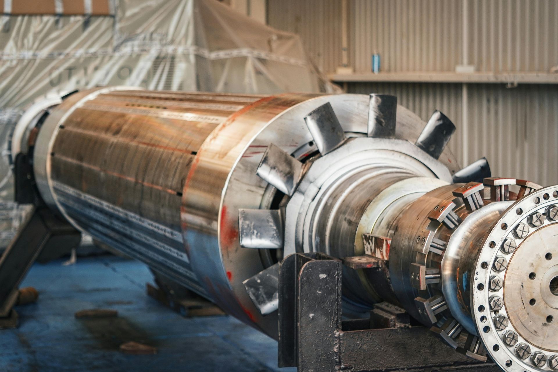 Large cylindrical industrial rotor with copper windings in a workshop, mounted on a machine for maintenance