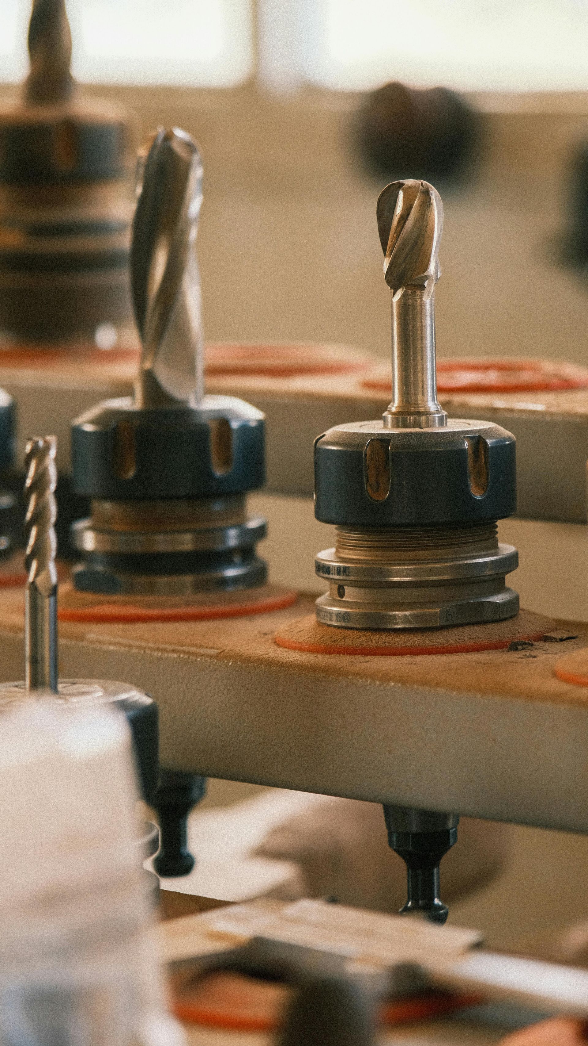 Close-up of metal drill bits or router bits mounted in a woodworking machine, with a blurred workshop background.