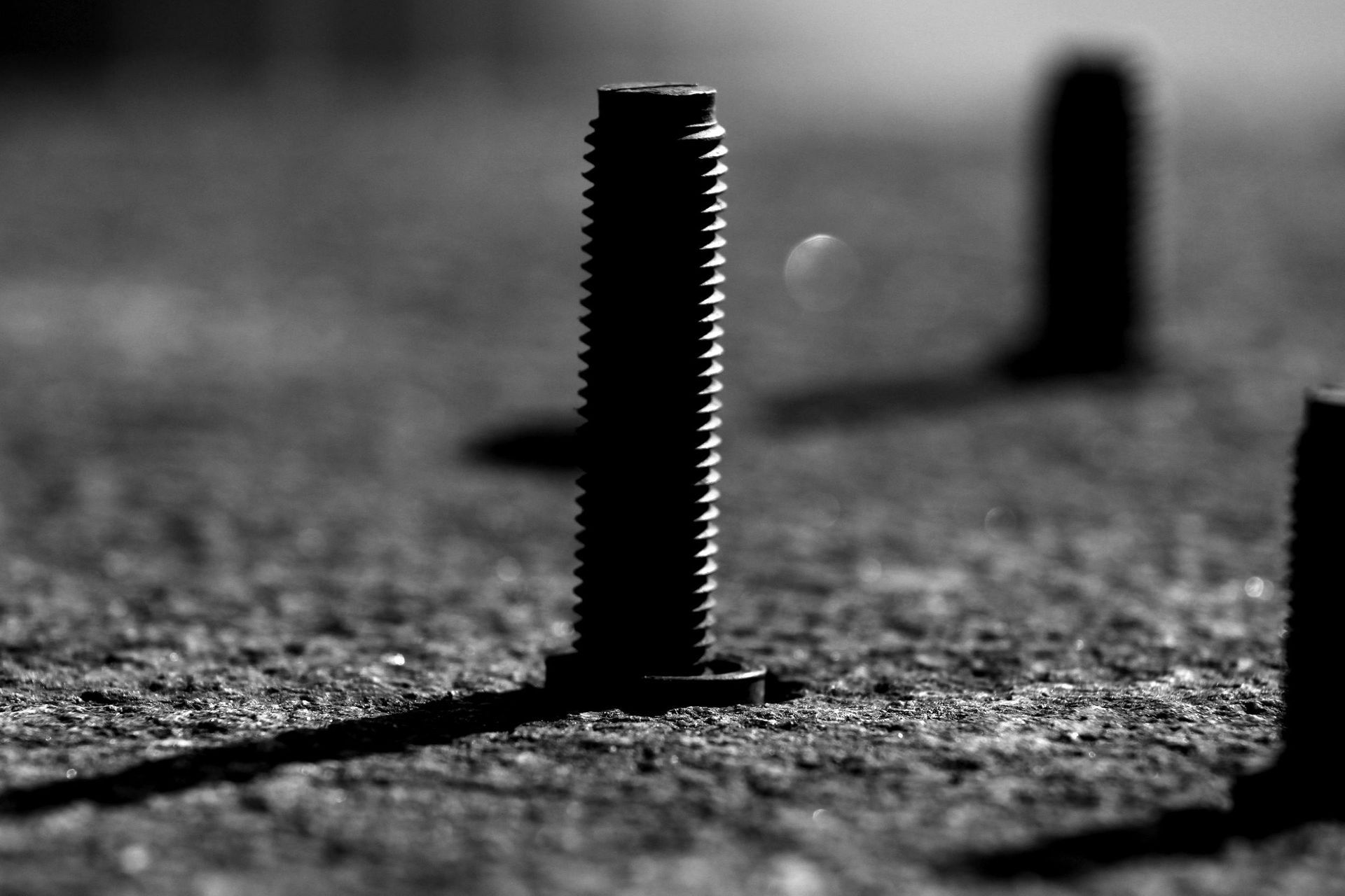 Close-up of a rusty bolt protruding from rough pavement, with blurred bolts in the background.