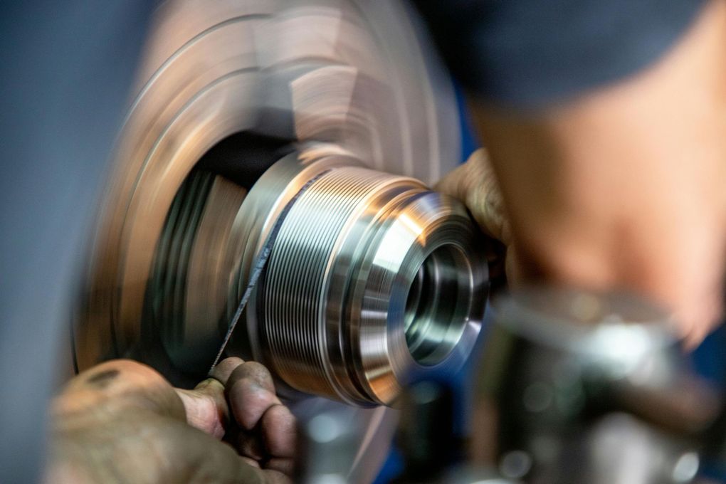Close-up of a metal lathe spinning a machined part with a worker’s hand in the background