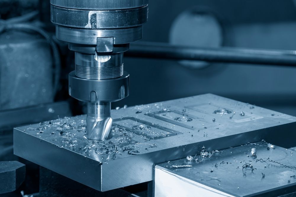 Metal milling machine cutting a steel block, with chips scattered on the work surface.