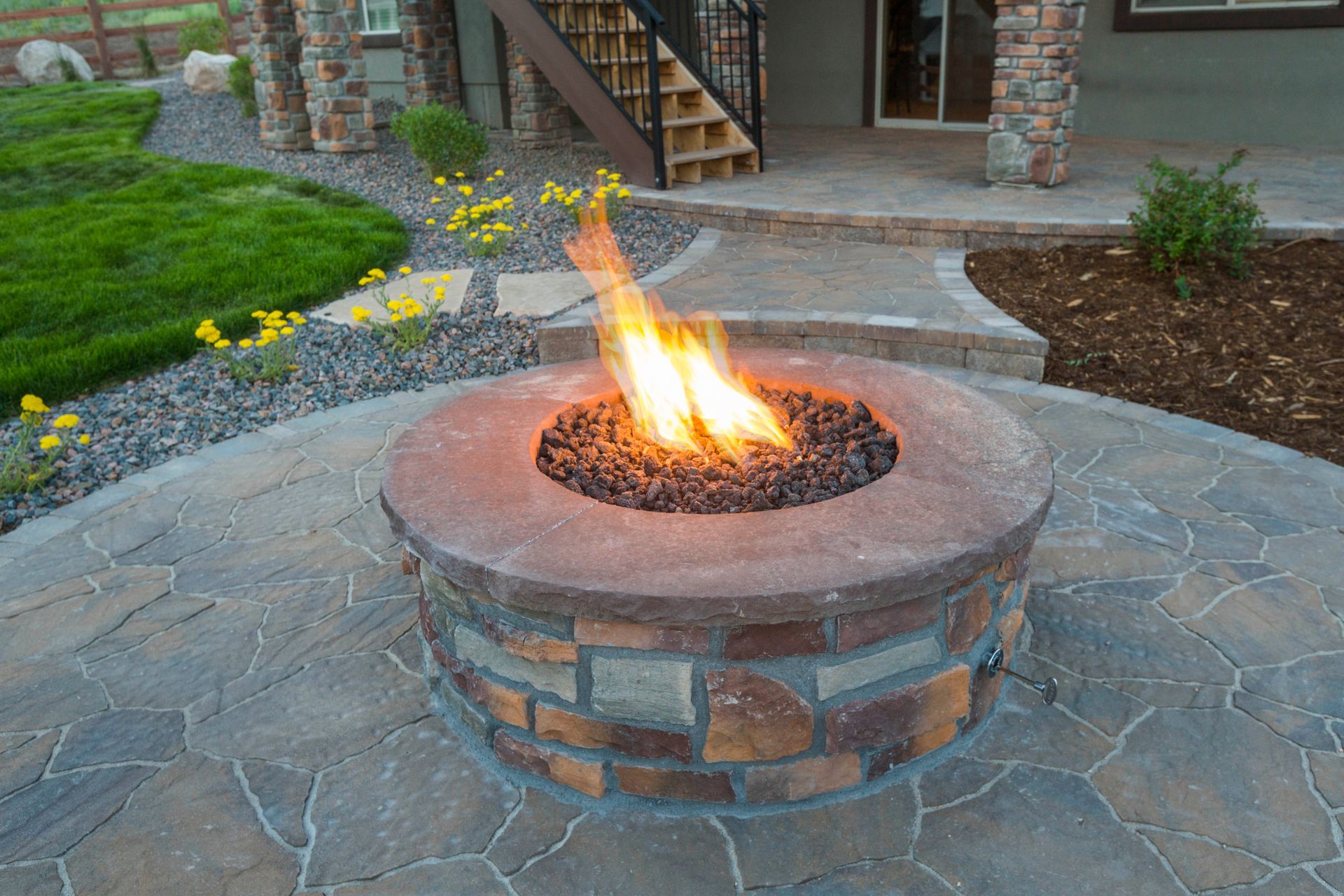 Stone backyard fire pit with a burning flame on a flagstone patio near a house entrance
