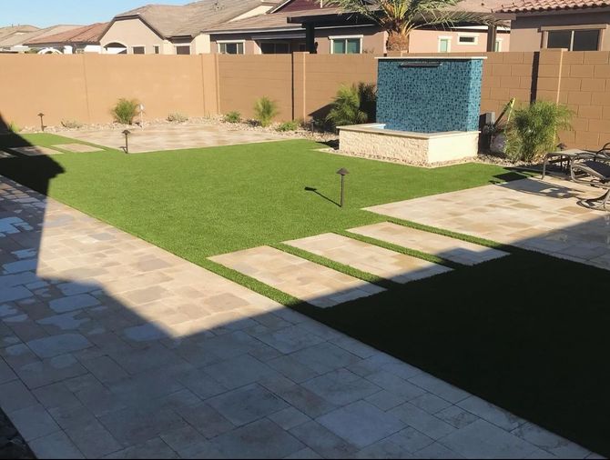 Backyard with green lawn, stone walkway, tan wall, and a blue-tiled water feature under bright sun