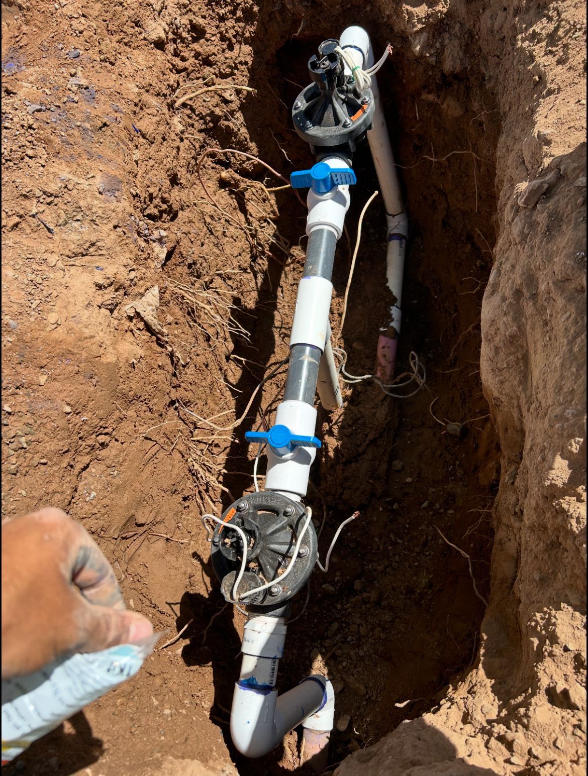 Trench with PVC pipes and blue valves being installed underground outdoors