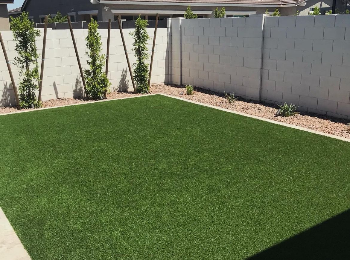 Backyard with bright green artificial turf, white block walls, and small planted border beds