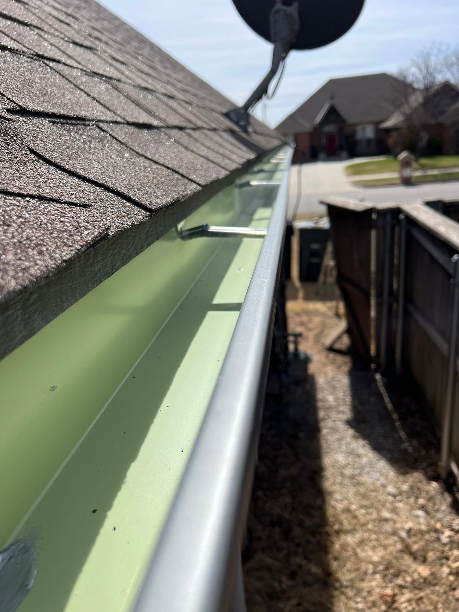 Green gutter installed along a shingled roof edge on a house under construction