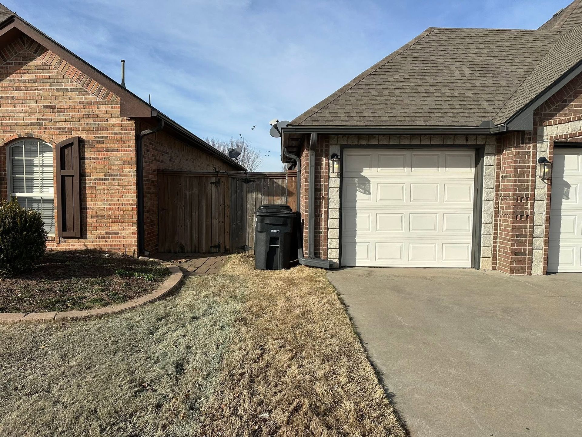Suburban brick houses with a driveway, garage, trash bins, and a dry front lawn