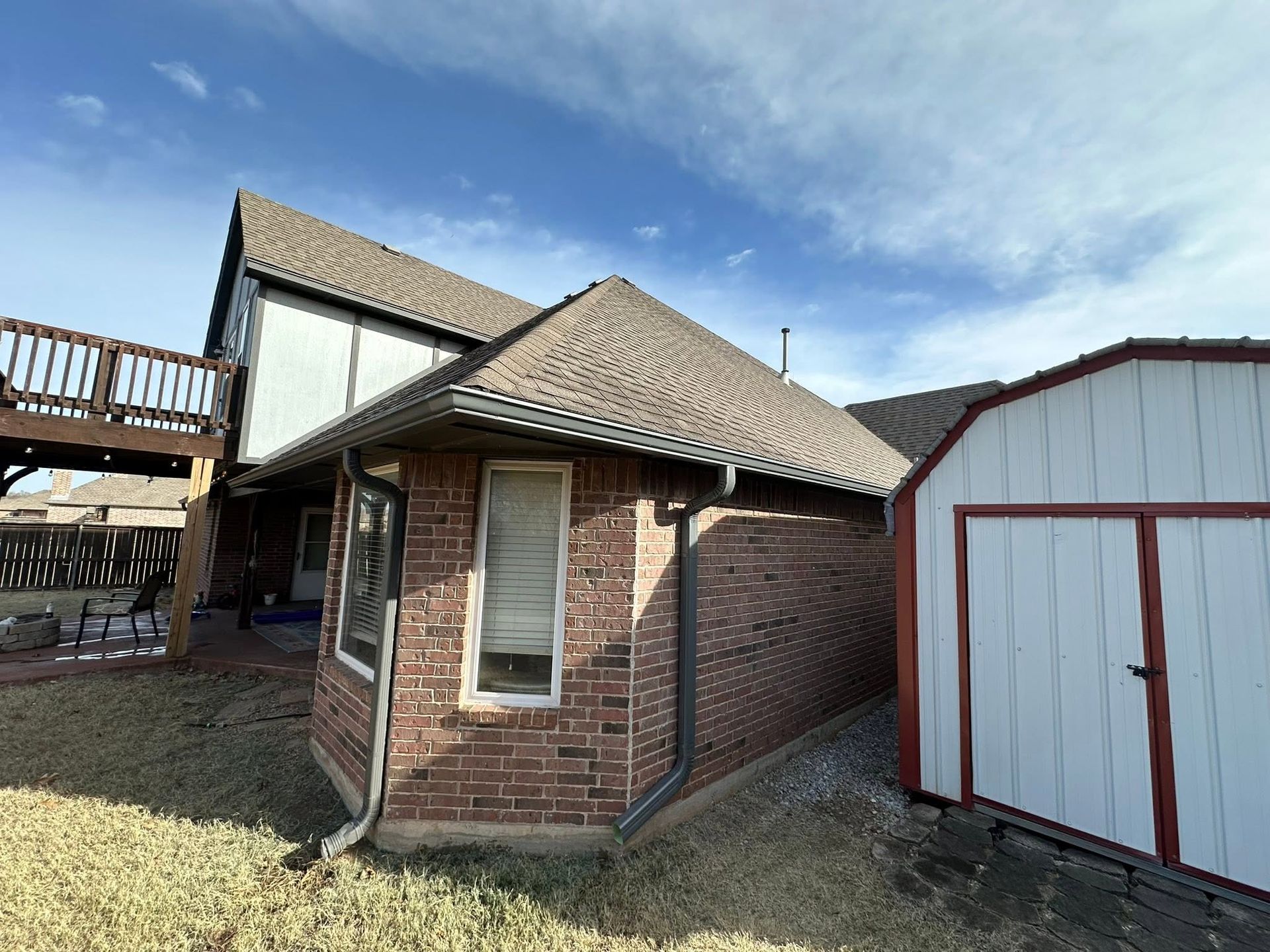 Brick house exterior with gabled roof beside a white and red shed under a blue sky