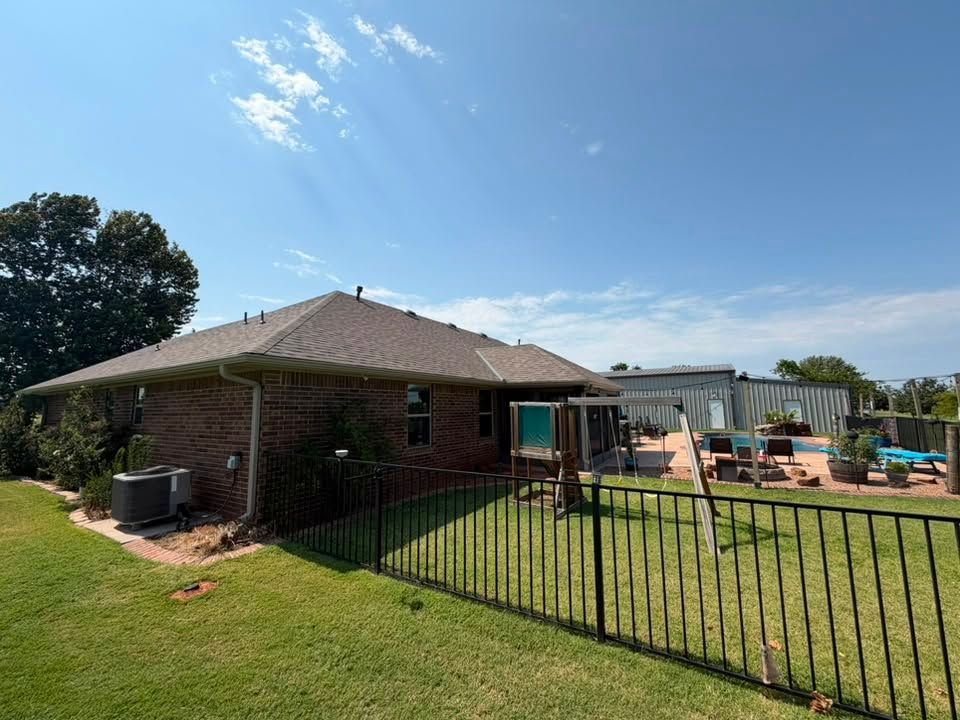 Brick house with fenced backyard, patio furniture, and grassy lawn under a blue sky