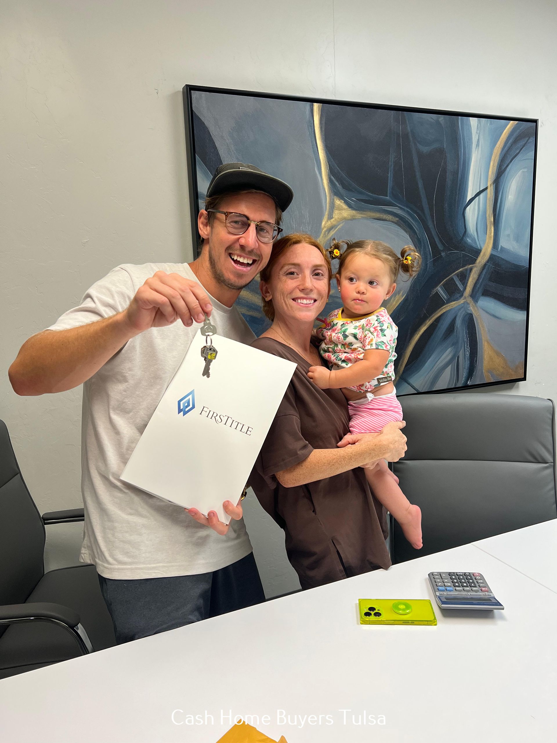 A family celebrating a new home purchase by holding keys and a folder in an office.