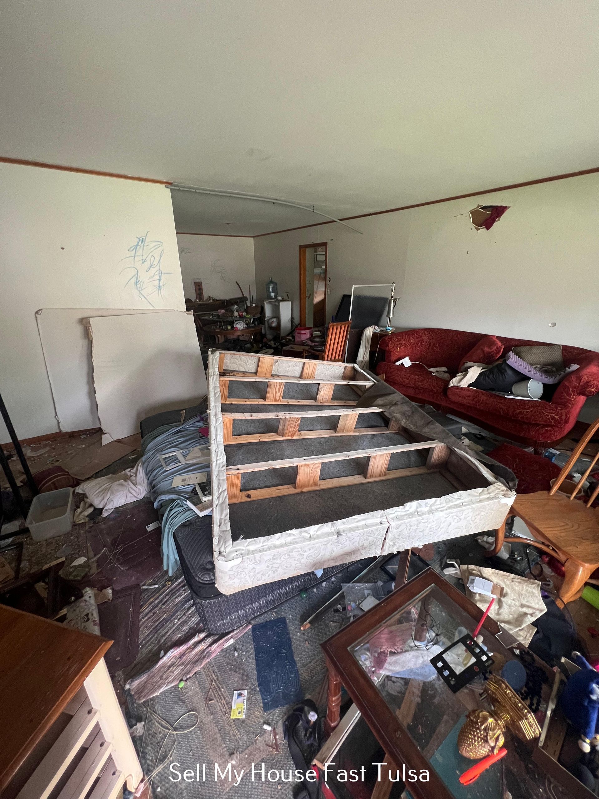 Damaged living room with debris, broken furniture, and a red couch against the wall.