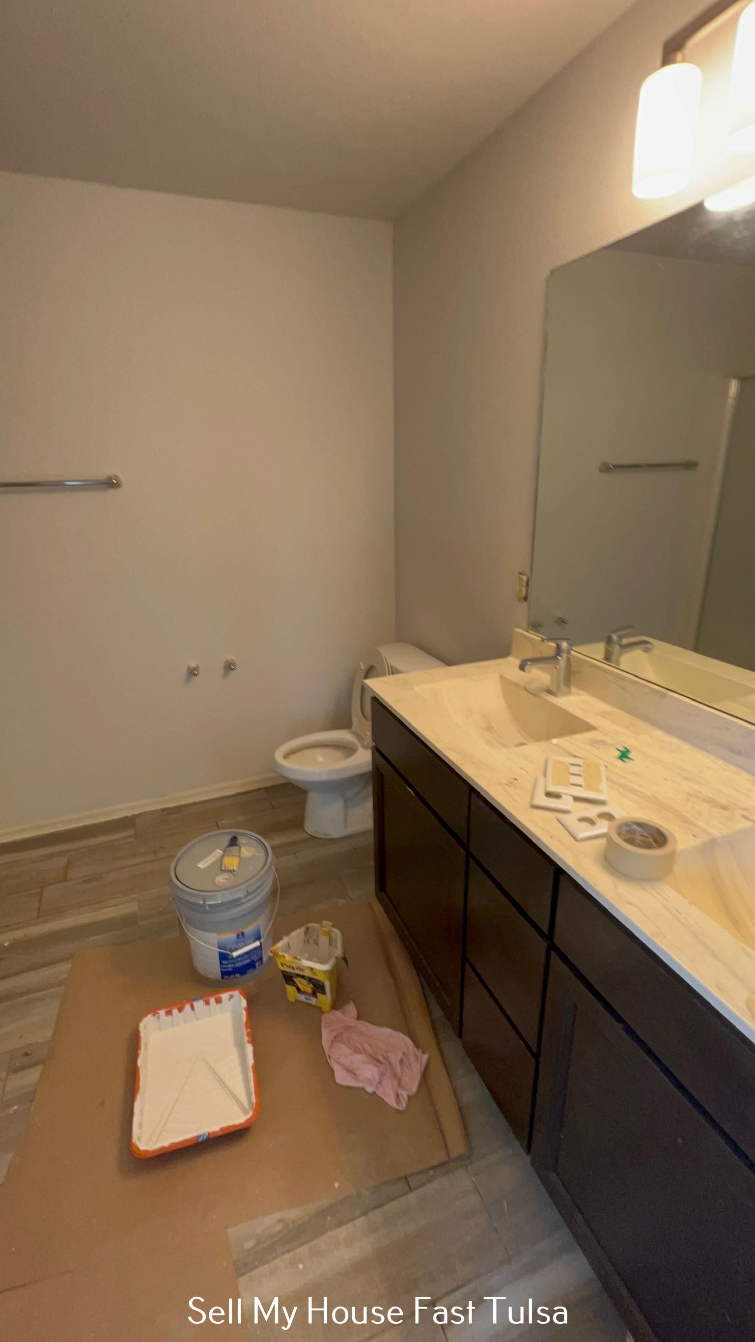 Bathroom under renovation with vanity, mirror, toilet, and tools on the floor.