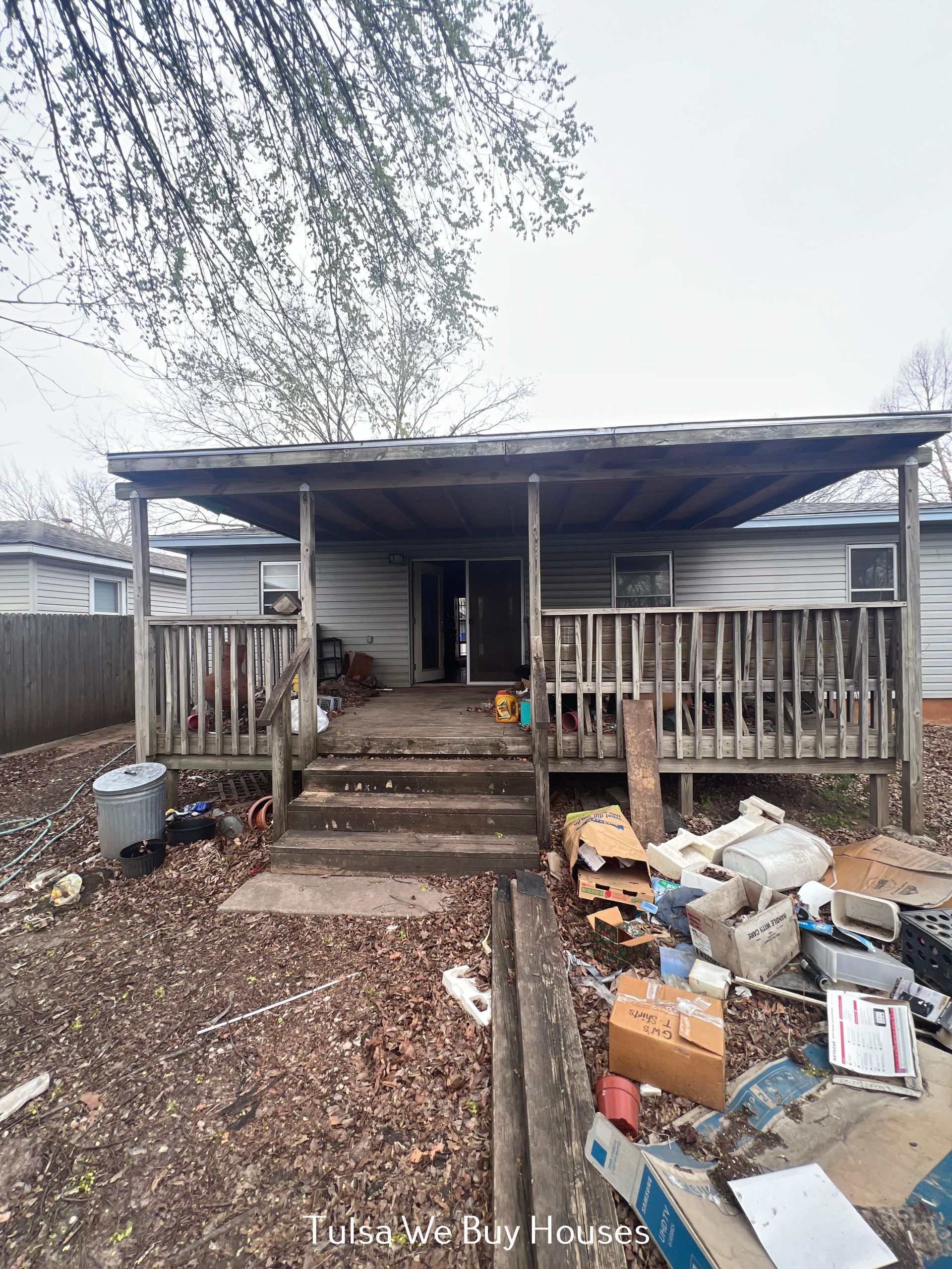 A wood-framed house with a covered porch and deck, surrounded by scattered debris and fallen leaves in the yard.
