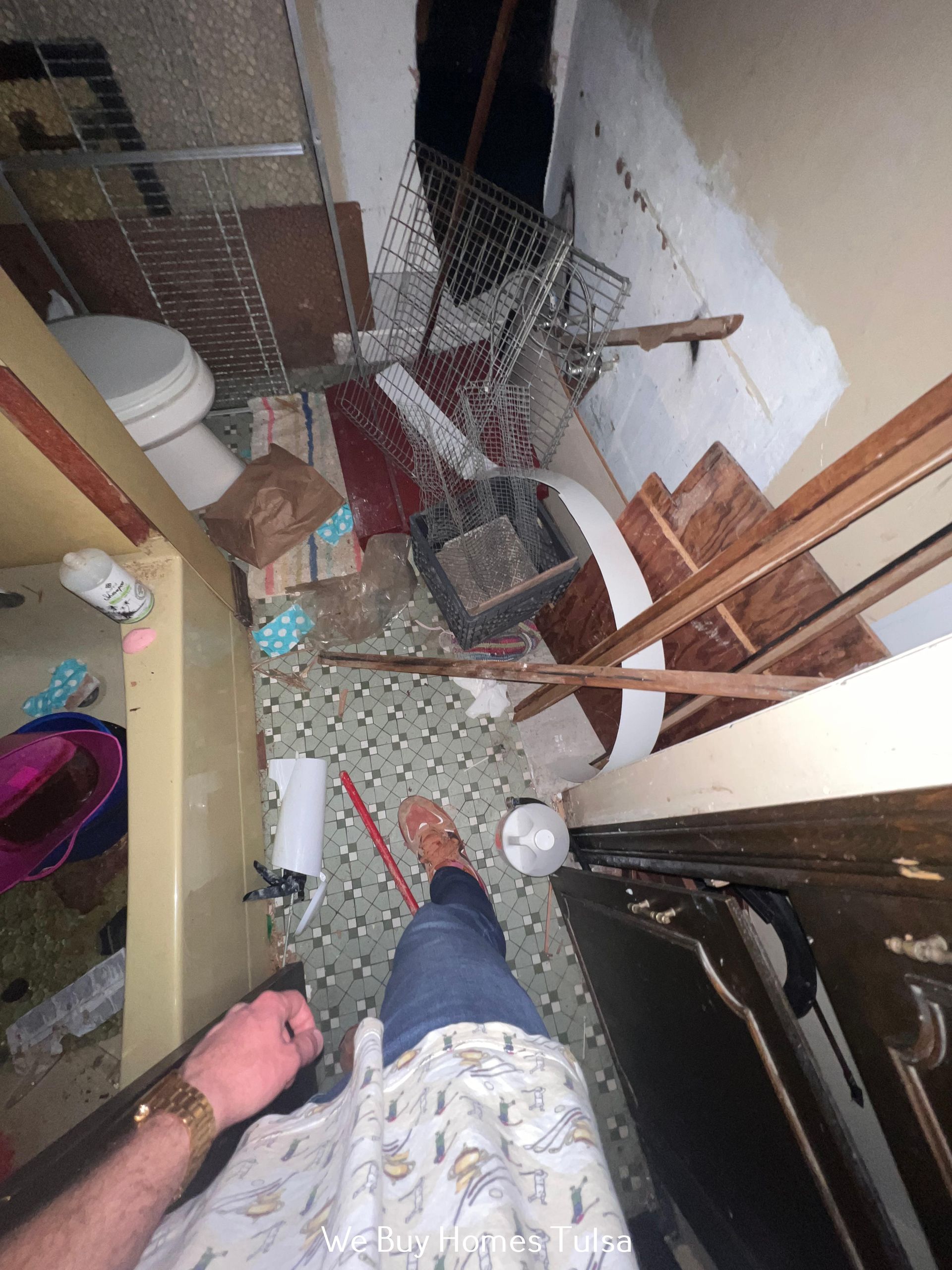 A person stands in a cluttered, under-construction bathroom with tiled floors, a toilet, debris, and bare wall studs.
