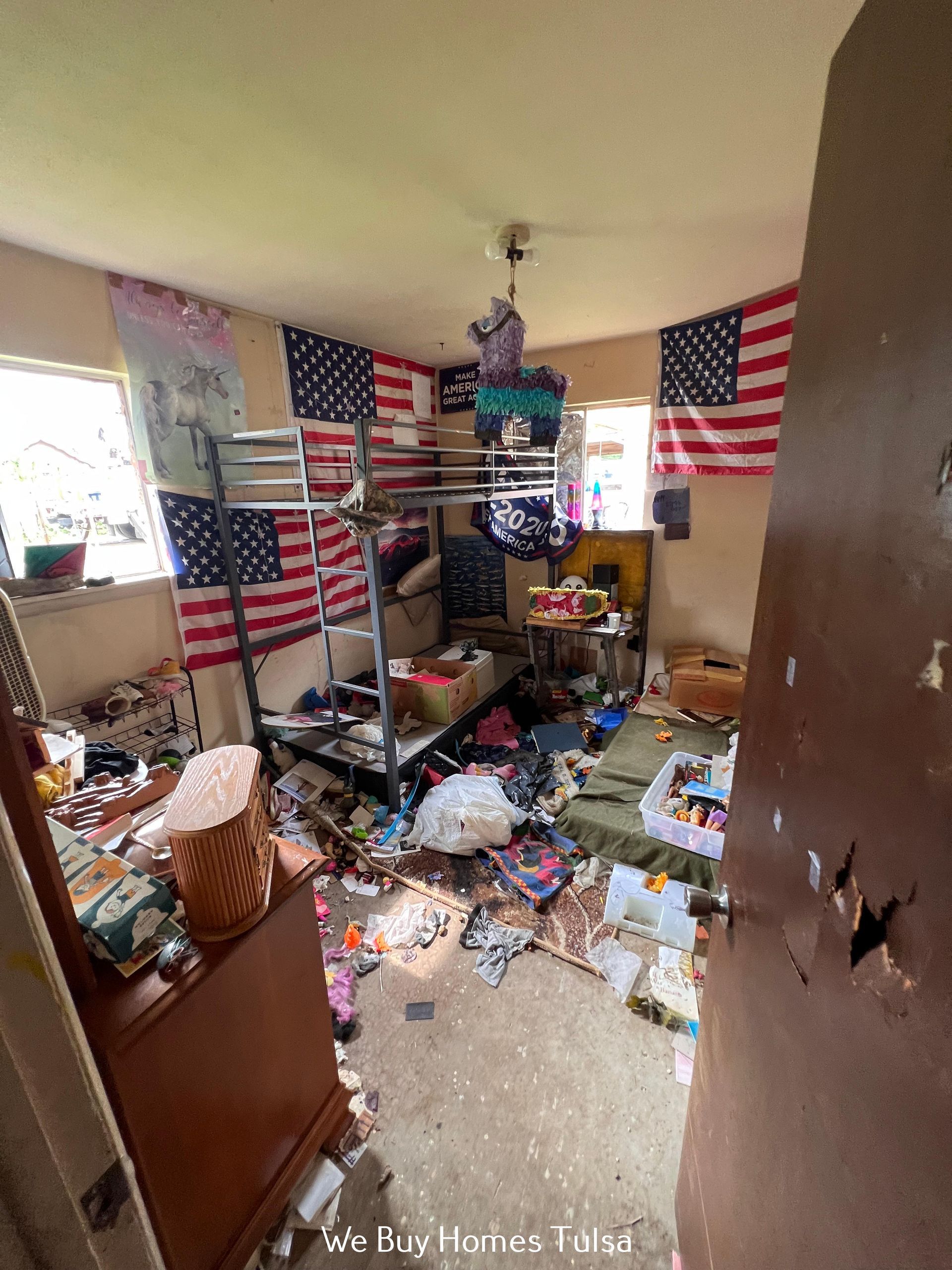 A cluttered bedroom with bunk beds, an American flag tapestry on the wall, and debris scattered across the floor.