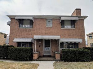 A two-story red brick apartment building with metal awnings over the windows and a central front entrance.