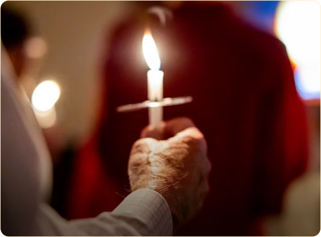Hand holding a lit candle during a candlelight vigil, with blurred people in the background