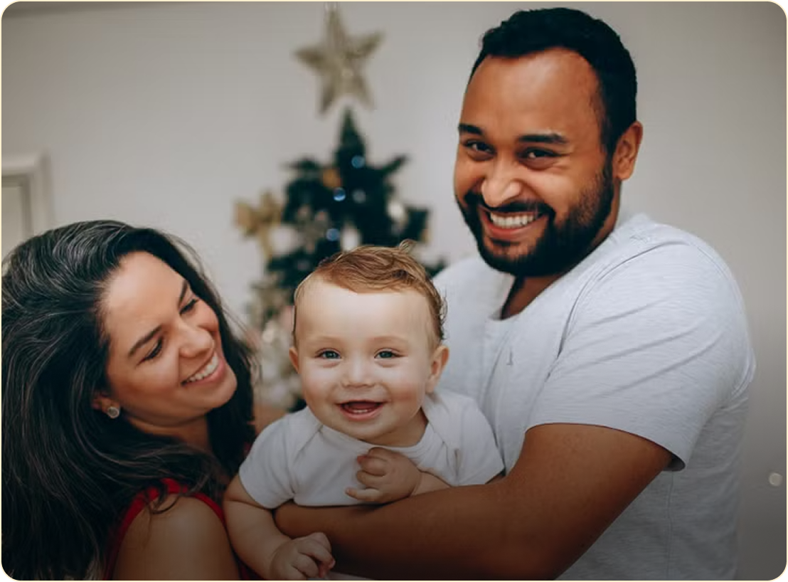 Smiling family holding a baby indoors with a Christmas tree in the background