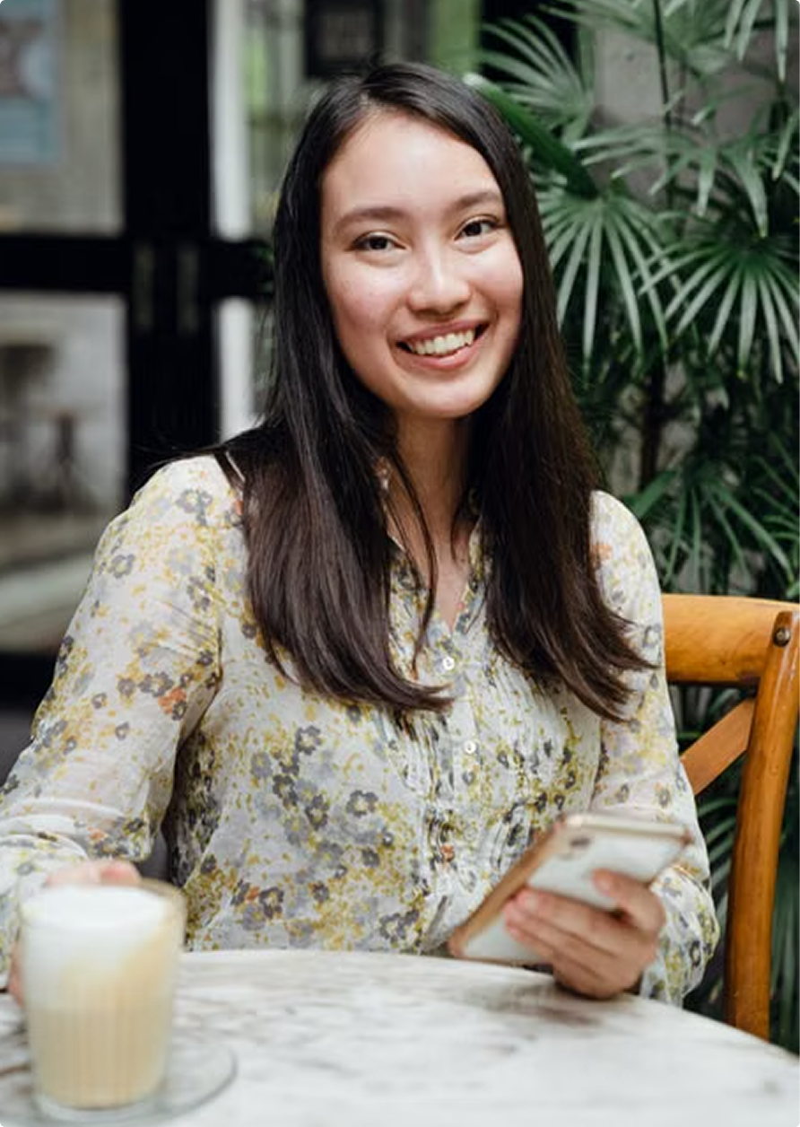 Smiling woman at a café table holding a phone, with a latte in front of her.