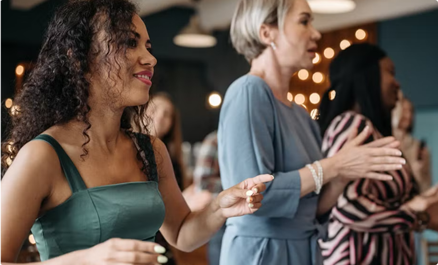 People holding drinks and clapping at a social gathering with warm lights in the background