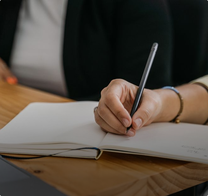 Hand writing in an open notebook at a wooden table with a pen, close-up view