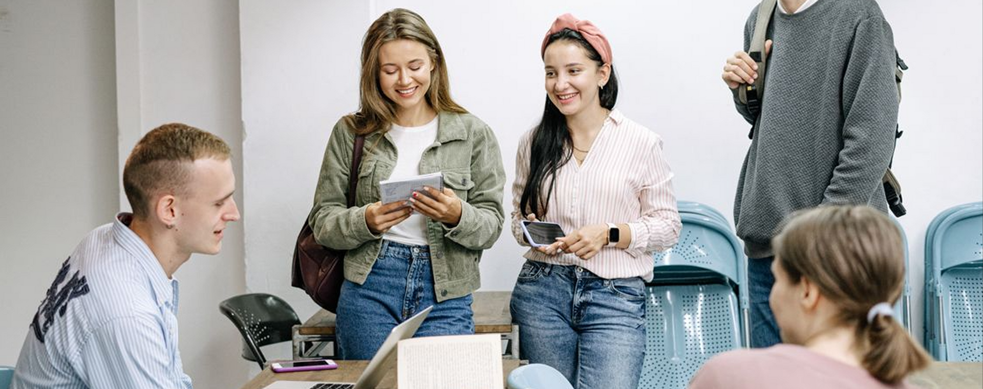 Group of people chatting and smiling in a bright office, some holding papers and phones.