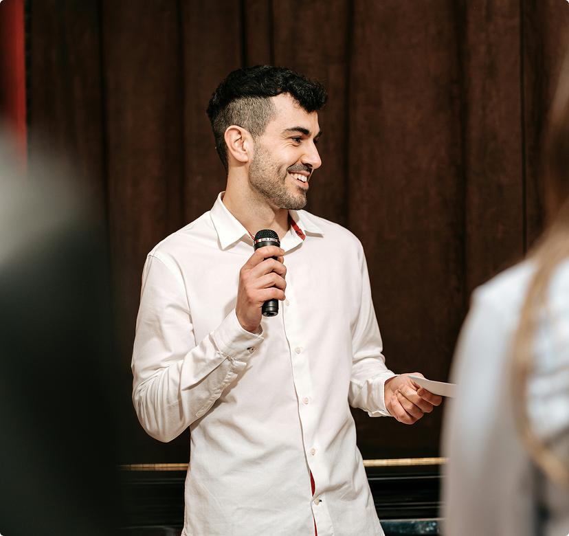 Man in a white shirt speaking into a microphone at an indoor event