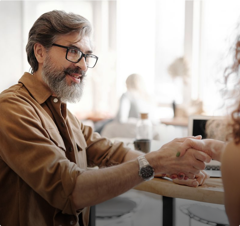 Smiling man in glasses and a brown jacket shakes hands across a café table