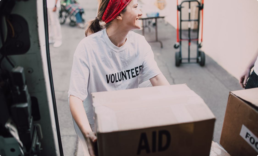 Volunteer in red headscarf carrying aid boxes at a relief distribution site