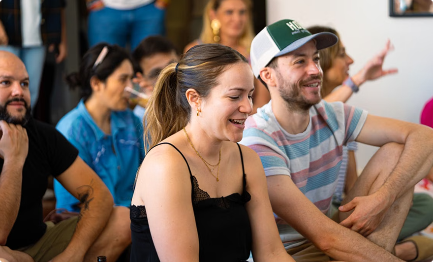 People seated indoors, smiling and listening in a casual group setting.