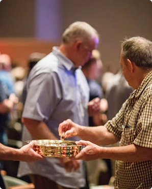 Two people exchange a small woven basket at a crowded indoor event.