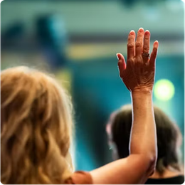 Person raising a hand in a blurred crowd, likely at a conference or event