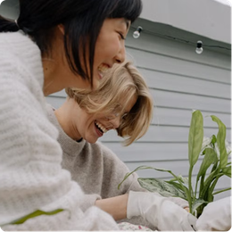 Two people smiling and tending a potted plant on a patio