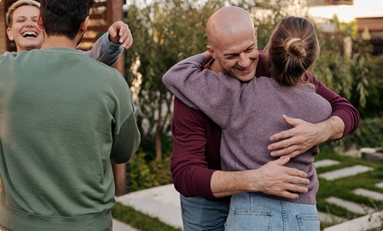 Two people hugging in a backyard while another person smiles nearby, with a house in the background