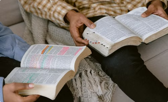 Two people reading open Bibles on a couch, one with highlighted passages