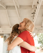 Two people in a warm embrace, smiling under a white-beamed ceiling outdoors.