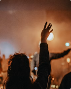 Silhouetted person raising a hand at a warm, orange-lit concert crowd at night