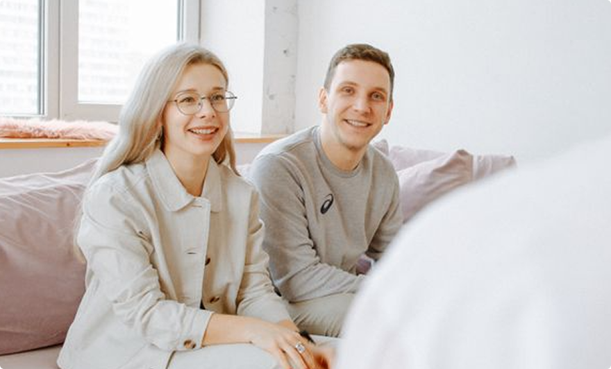 Two people smiling on a bed in a bright, cozy bedroom