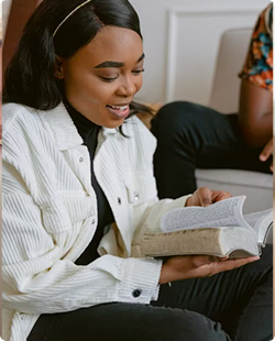 Person in a white shirt reading a book on a couch, smiling and seated indoors