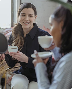Two friends chatting over coffee on a couch, one smiling and holding a cup
