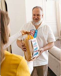 Person receiving a grocery bag from another person in a bright living room