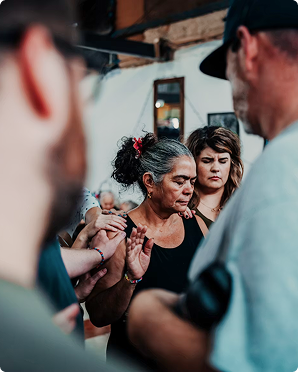 People gathered closely around a woman with gray hair and a black top in an indoor setting