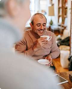 Smiling man in a brown shirt drinking coffee in a cozy café