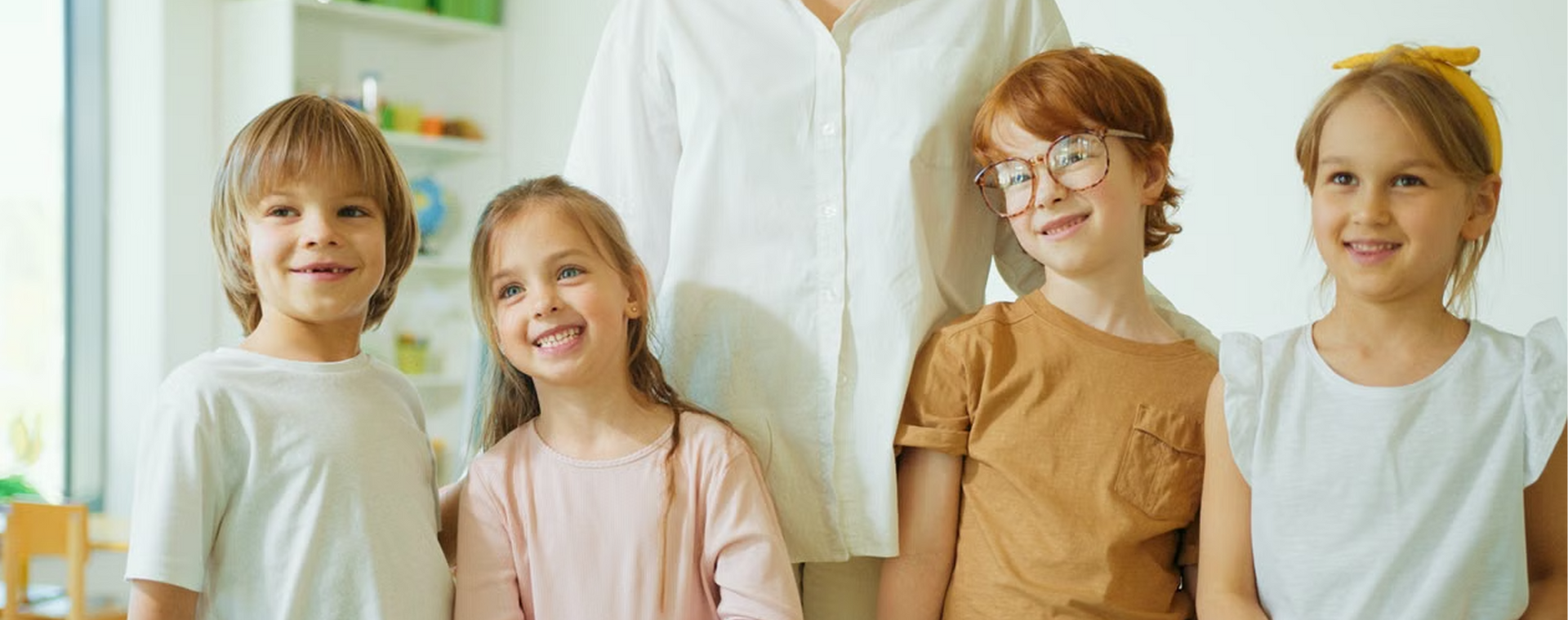 Four children standing indoors in front of hanging white clothes, smiling at the camera.