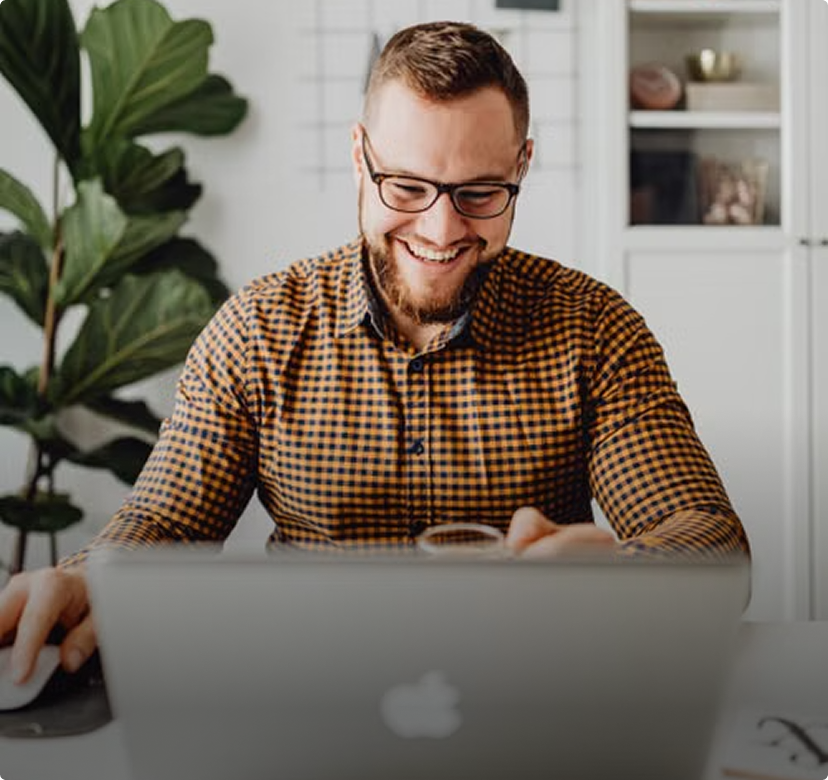 Smiling man in glasses using a laptop at a desk in a bright home office