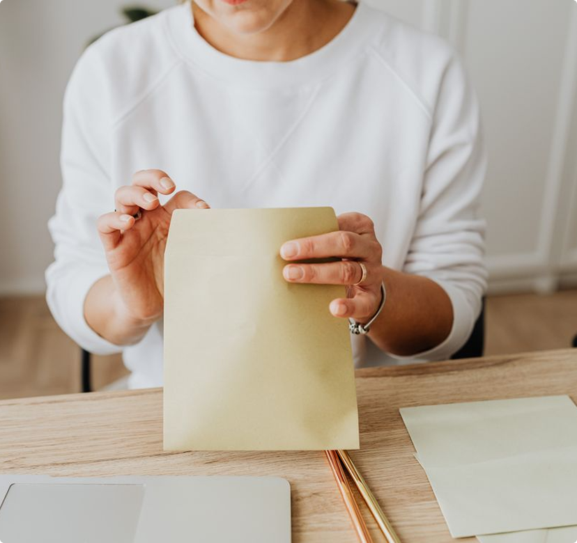 Person holding a cream-colored envelope at a wooden table with stationery and a pencil nearby