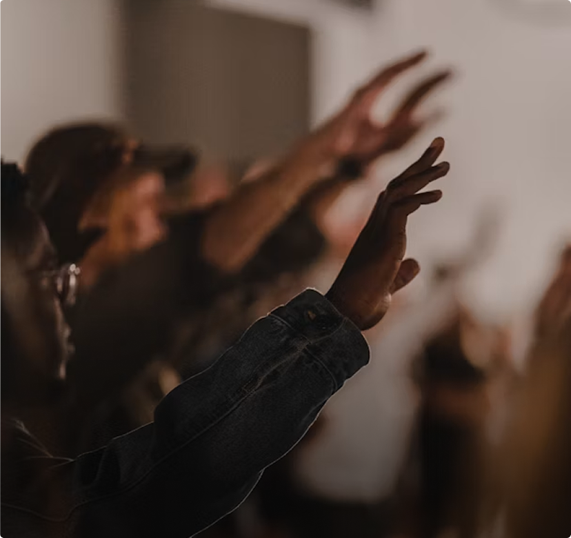 People raising hands in a dimly lit indoor gathering