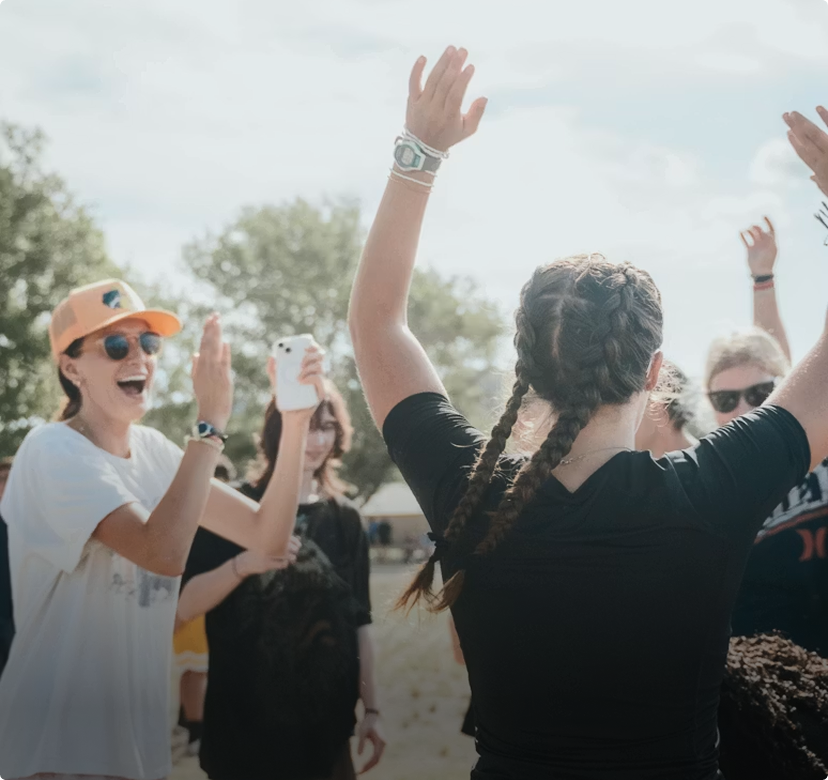 Crowd cheering outdoors with raised hands at a sunny event, one person holding up a phone